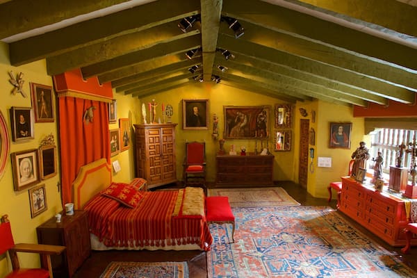 A traditional bedroom with a wooden ceiling, a large bed with red bedding, and various framed pictures and decorations on the walls.