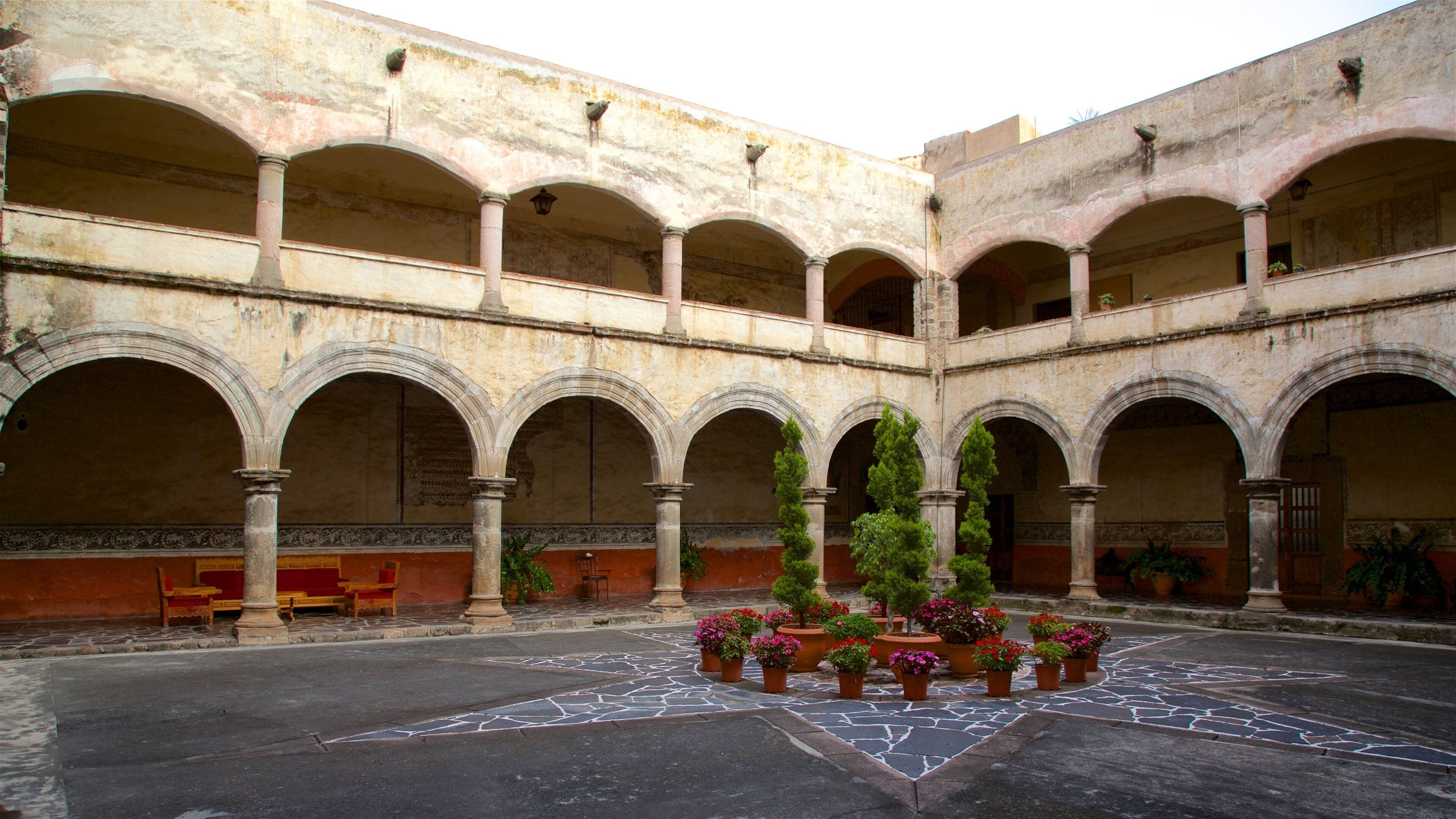 An ancient courtyard with arches, columns, and potted plants.