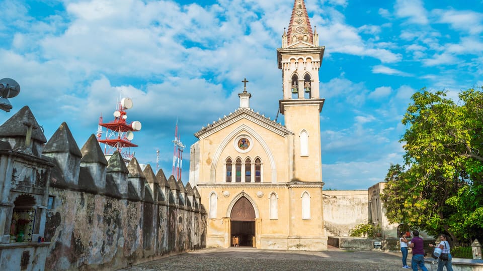 A historic church with a bell tower and a stone wall with pointed towers.