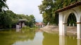 A calm river with a bridge, lush greenery, and a traditional building with a tiled roof.