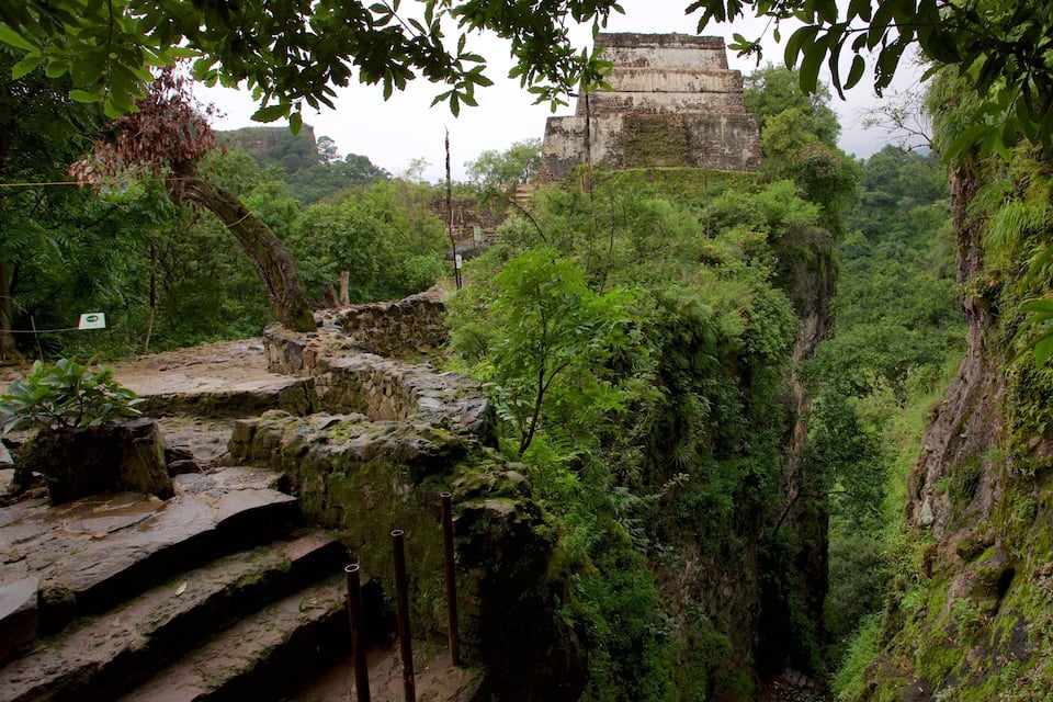 A stone staircase leading up a steep, moss-covered cliff with a large ancient temple in the background.