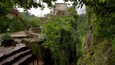 A stone staircase leading up a steep, moss-covered cliff with a large ancient temple in the background.