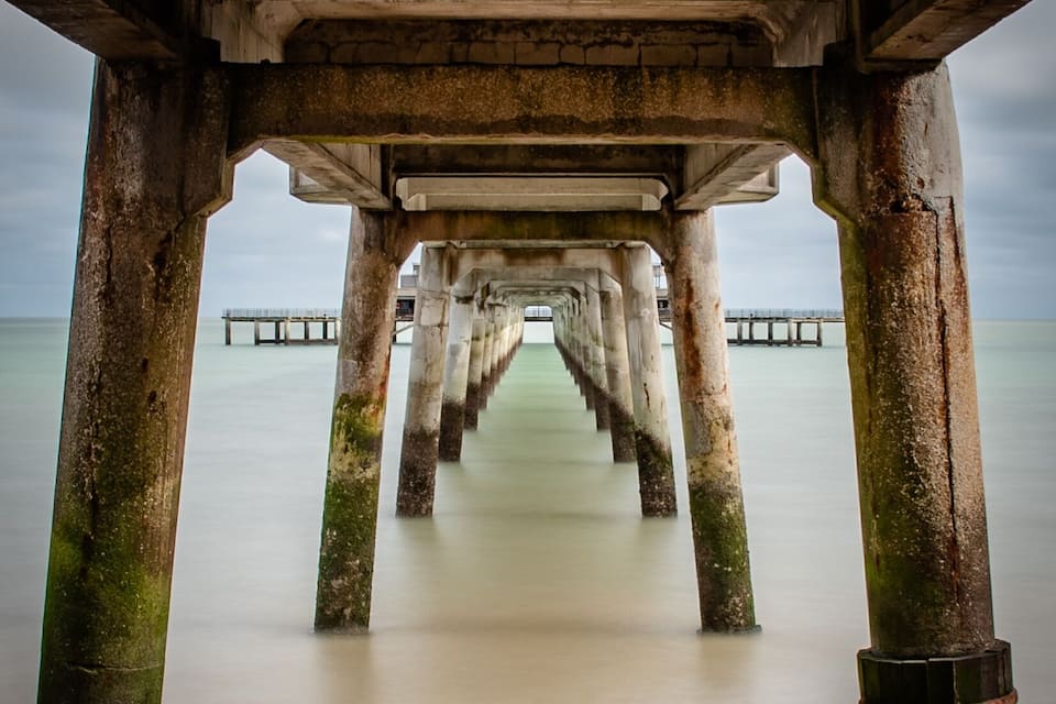 A pier extending into calm water, supported by rusted pillars.