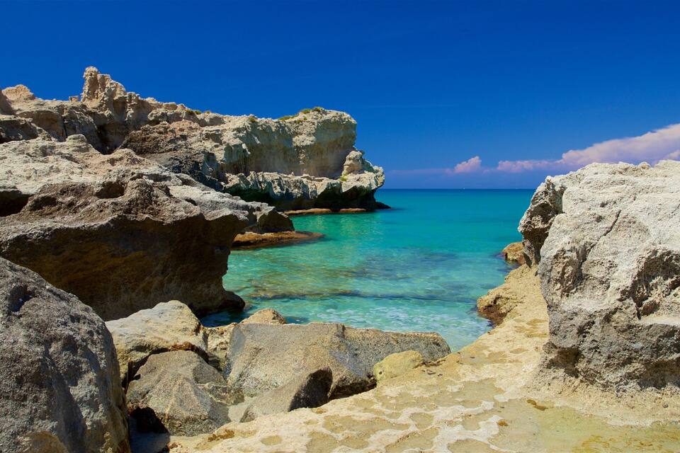 Eine felsige Küstenlinie mit klarem türkisblauem Wasser und blauem Himmel.