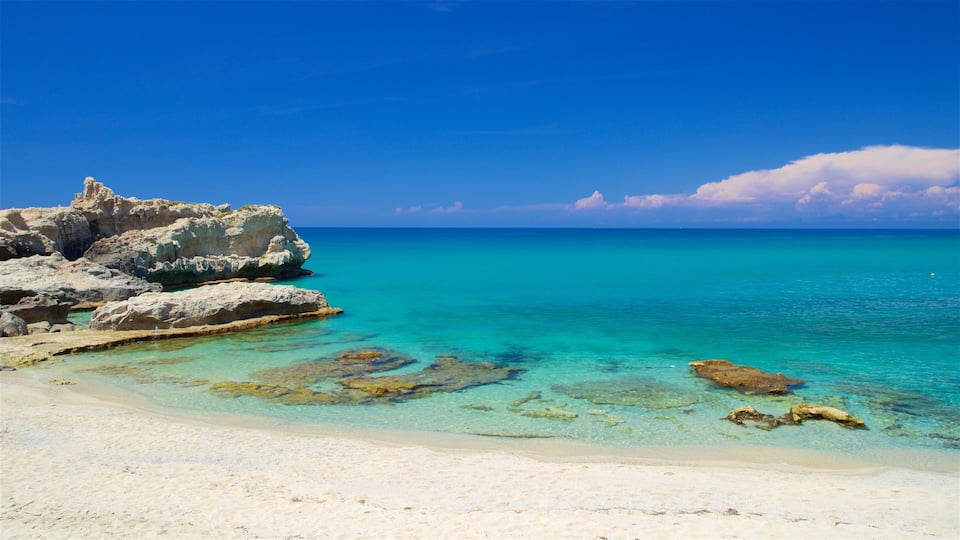 A beach with clear turquoise water, white sand, and rocky formations.