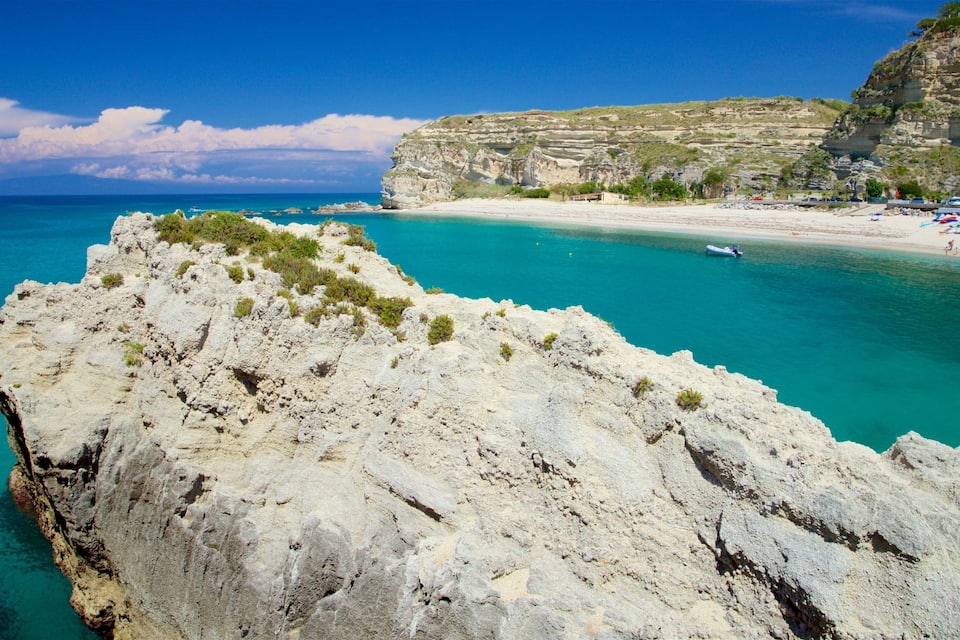 A rocky coastline with clear turquoise waters, a sandy beach, and a cliff with sparse vegetation.