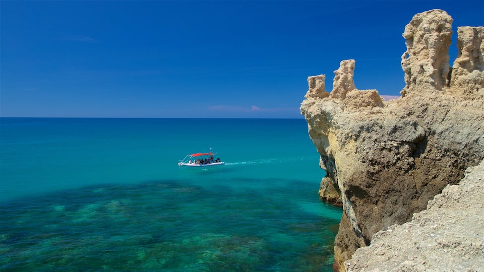 A boat on turquoise waters near a rocky cliff.