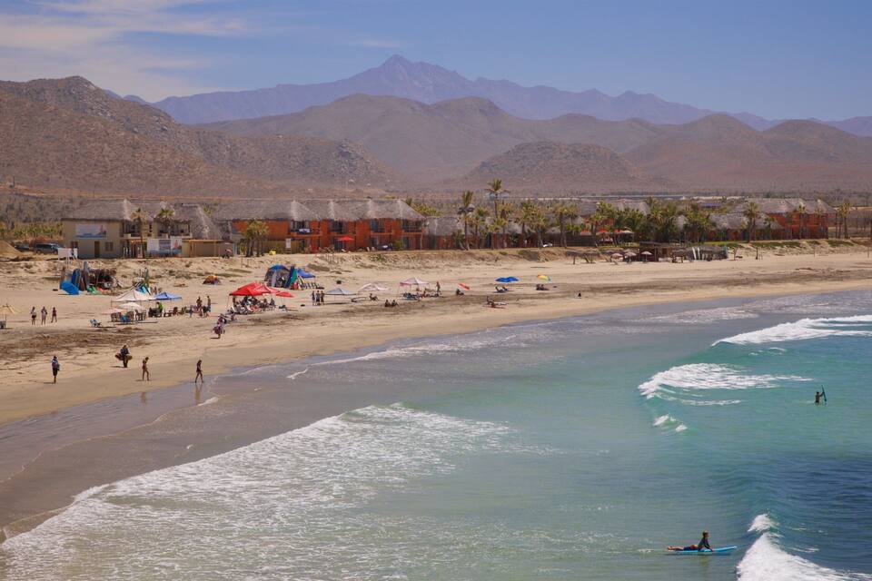 A beach with people, tents, and a mountain range in the background.