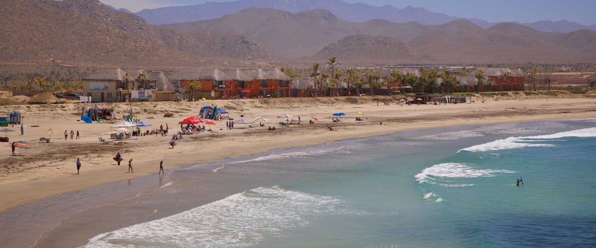 A beach with people, tents, and a mountain range in the background.