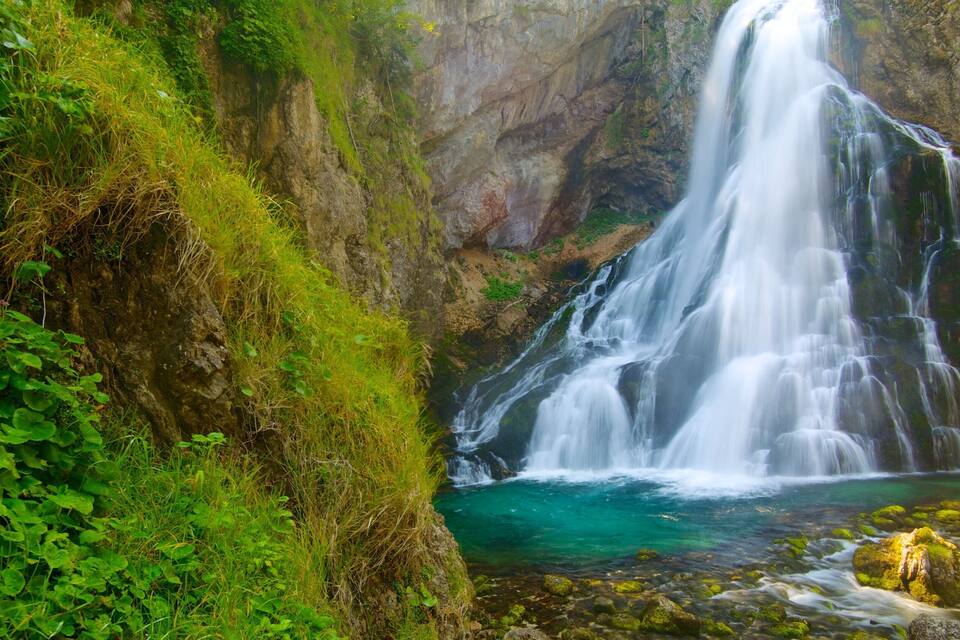 Une cascade se jetant dans un bassin d’eau claire, entouré d’une végétation luxuriante et de falaises rocheuses.