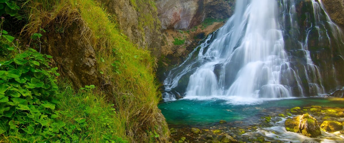 A waterfall cascading into a clear pool surrounded by lush greenery and rocky cliffs.