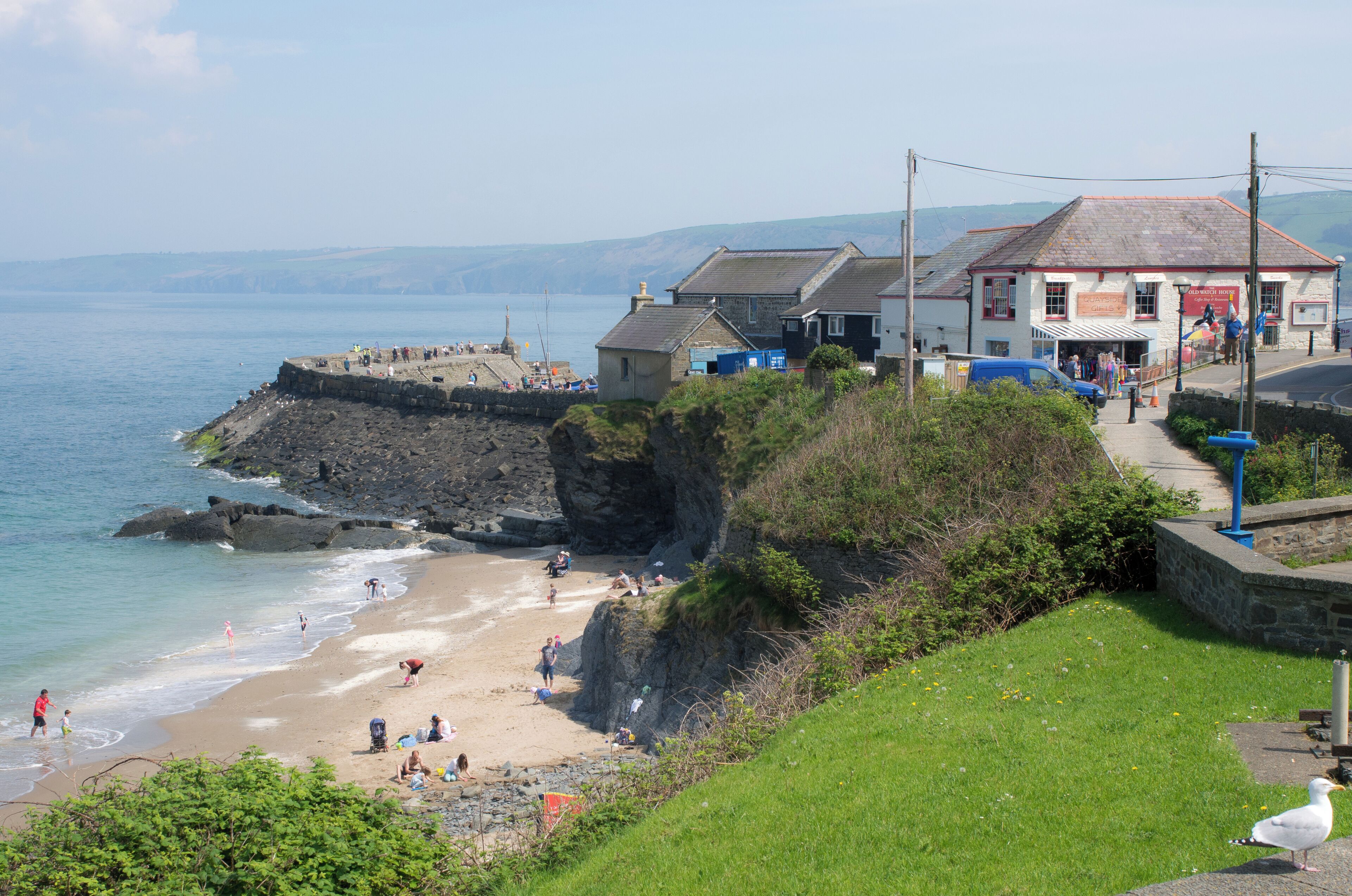 A coastal town with a beach, rocky cliffs, and a prominent building with a sign.
