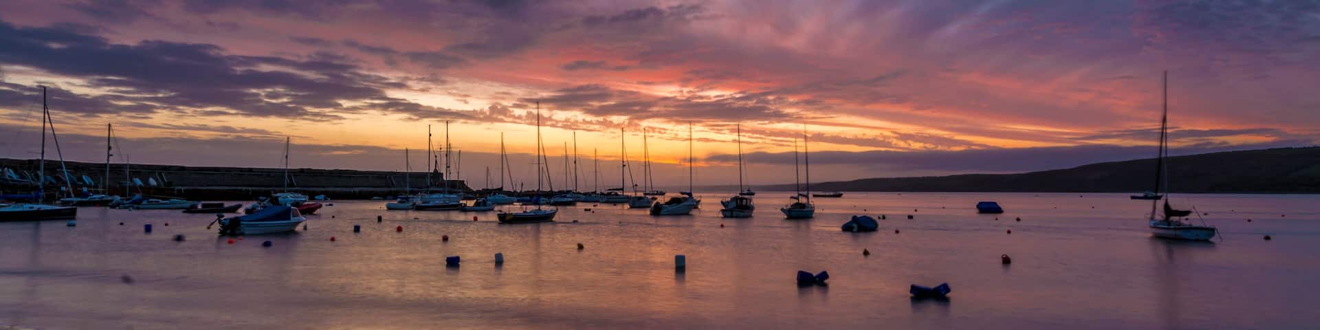 A marina at sunset with boats docked and a colorful sky.