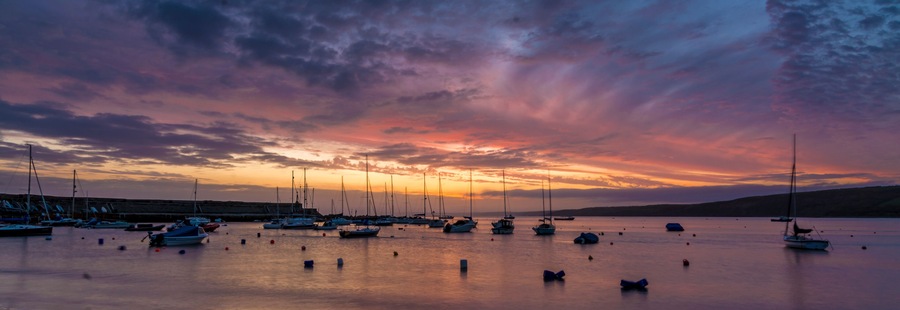 Un puerto deportivo al atardecer, con barcos amarrados y un cielo colorido.