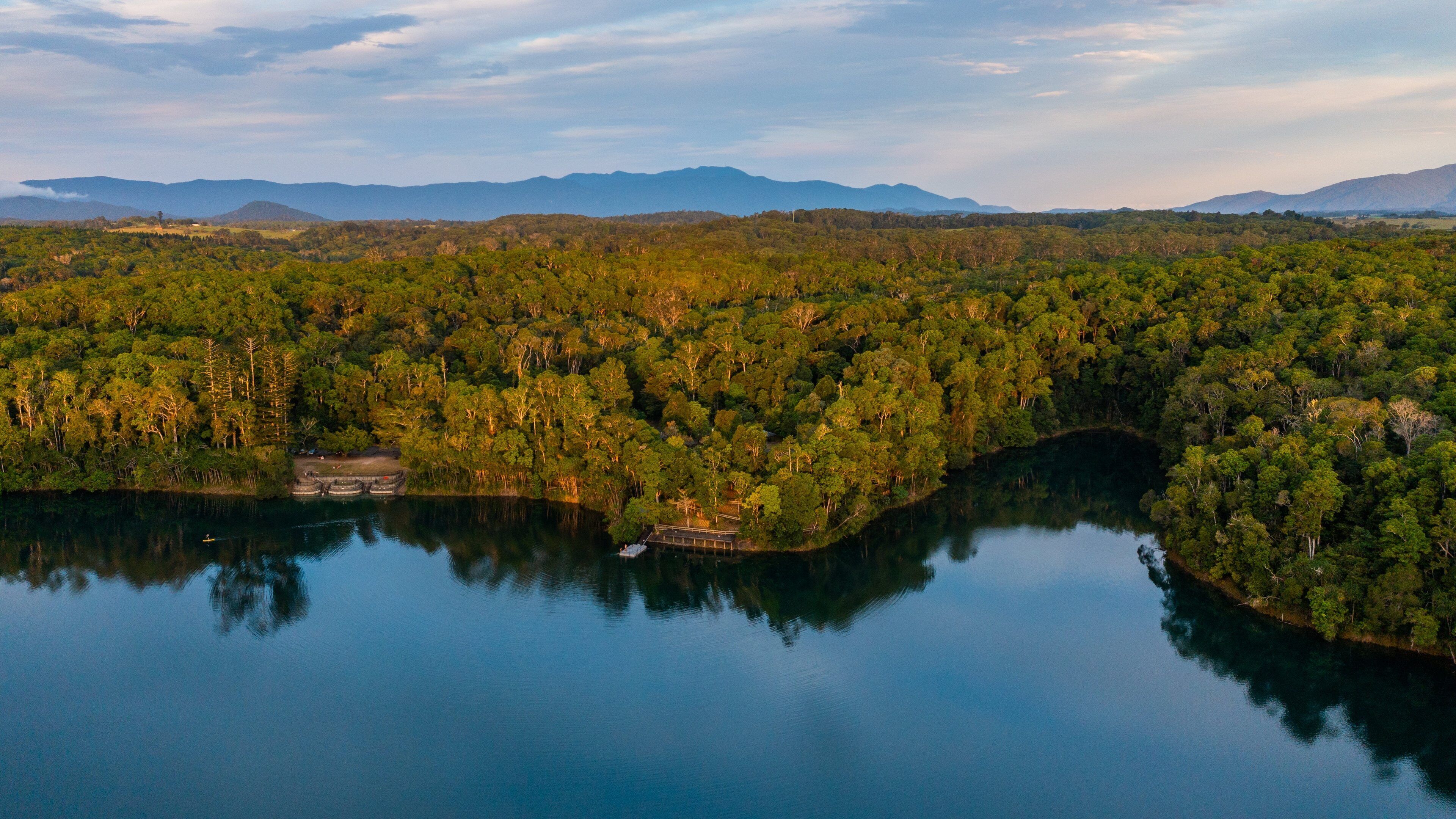 A lake surrounded by dense forest and mountains in the background.