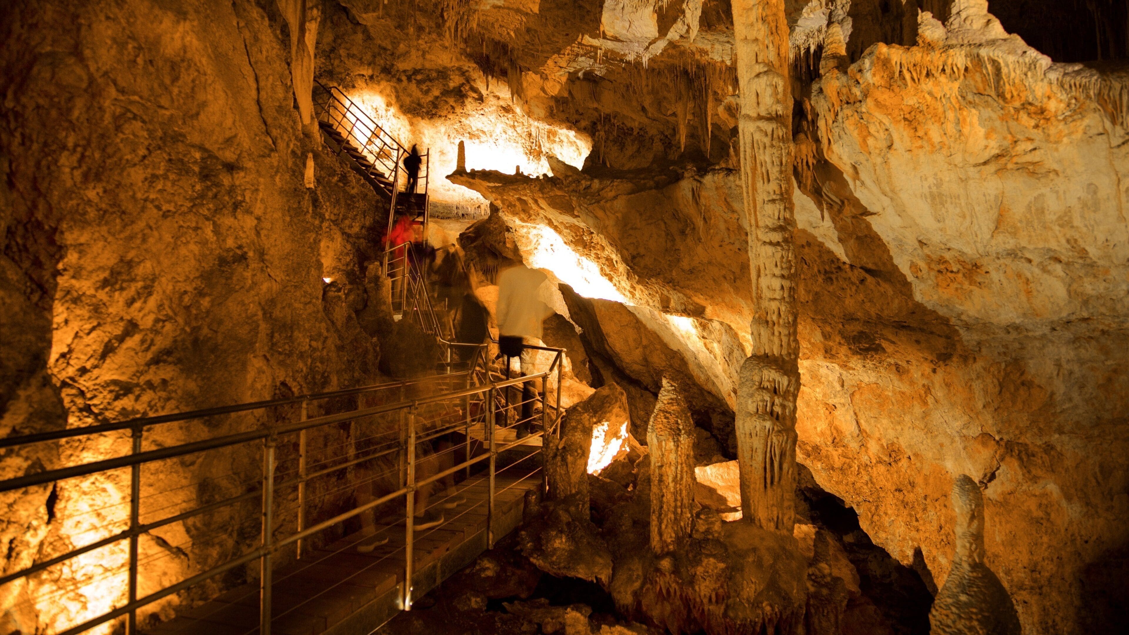 A cave with stalactites and stalagmites, metal railings, and a person climbing.
