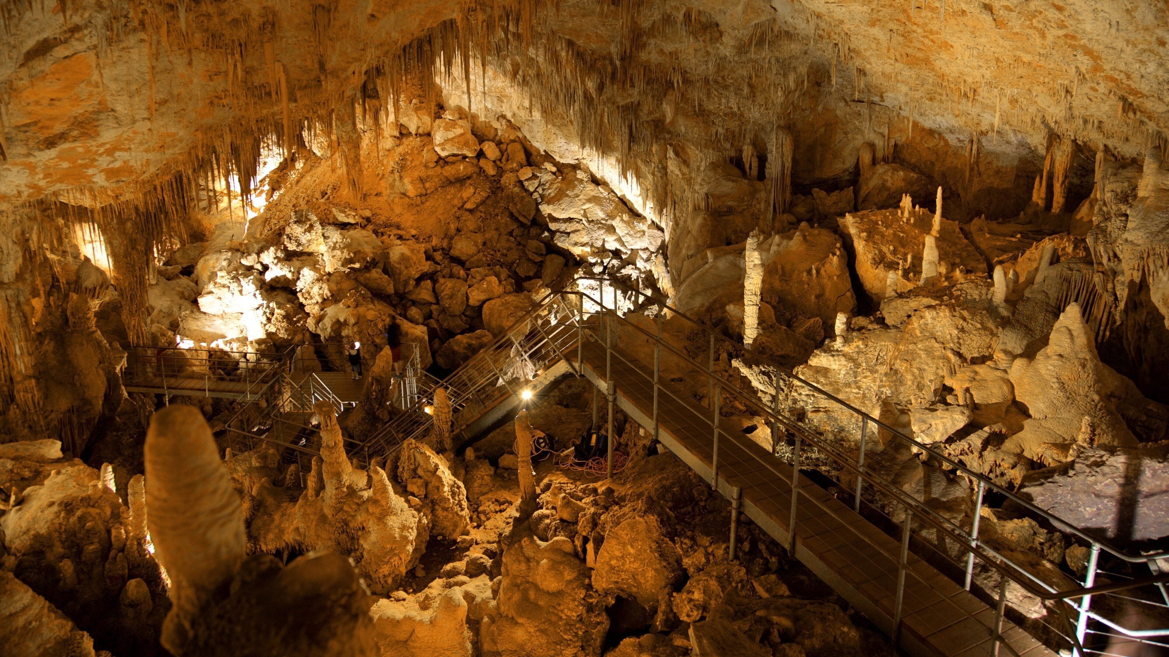 A cave with stalactites, a metal walkway, and a person standing on a platform.