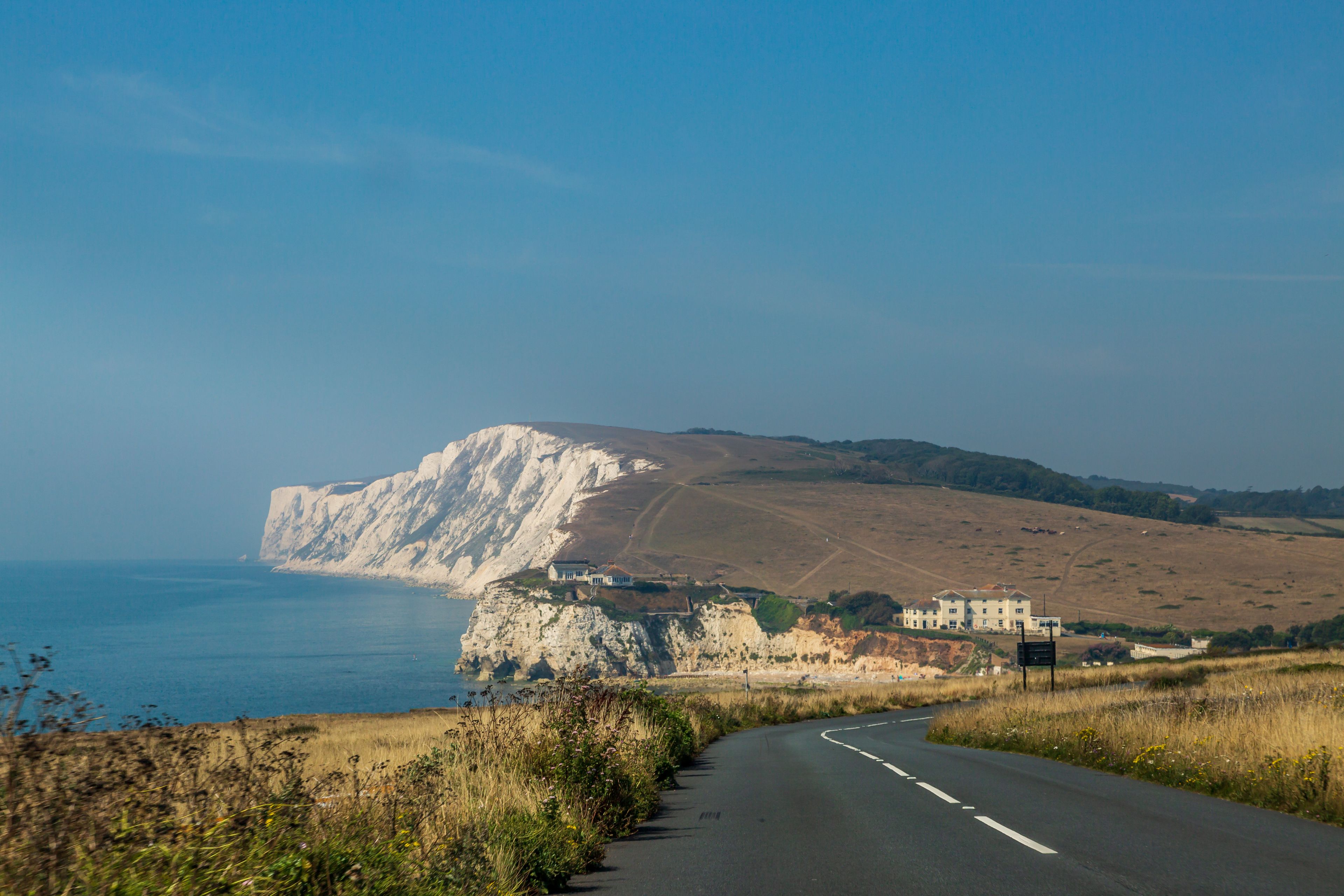 A coastal road with a cliffside view, a clear sky, and a distant building.