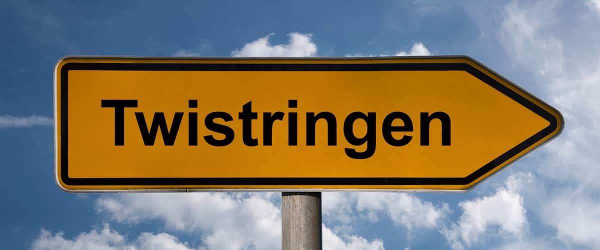A directional sign with the text "Twistringen" against a blue sky with clouds.