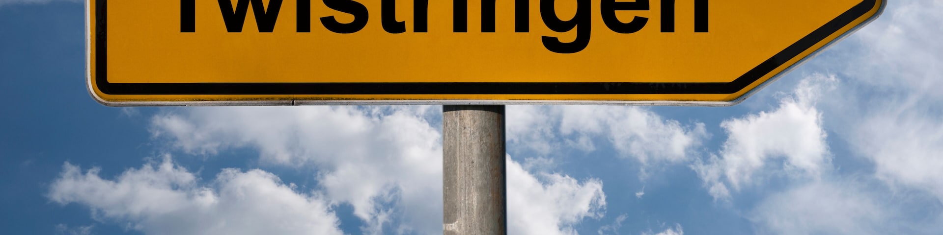 A directional sign with the text "Twistringen" against a blue sky with clouds.
