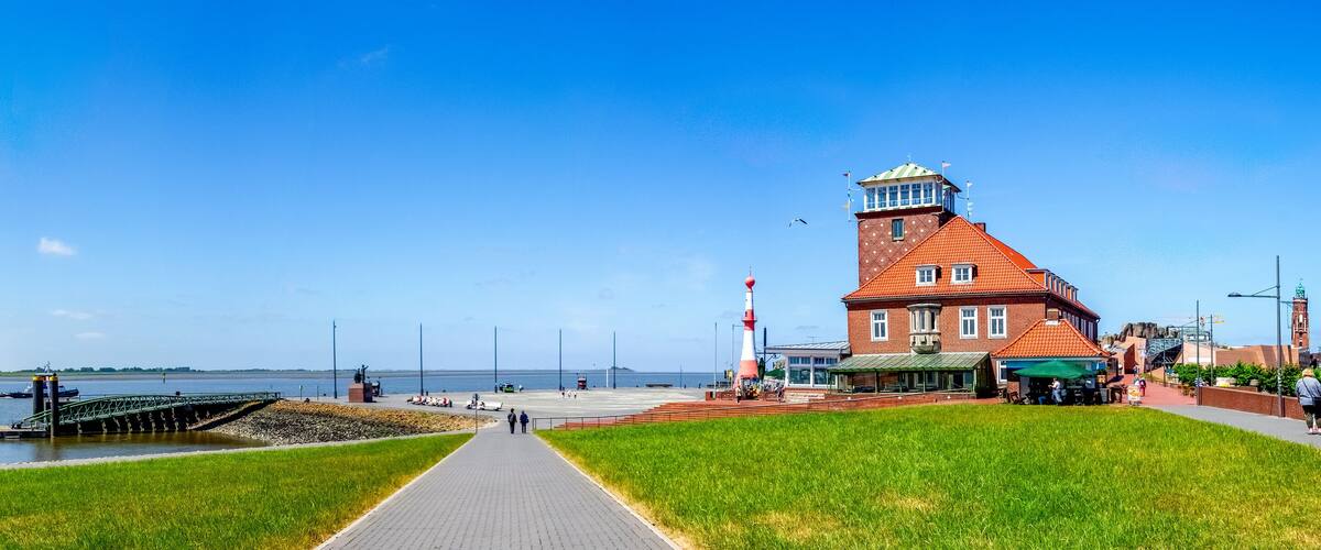 A waterfront promenade with a red brick lighthouse, a green pathway, and a calm river.
