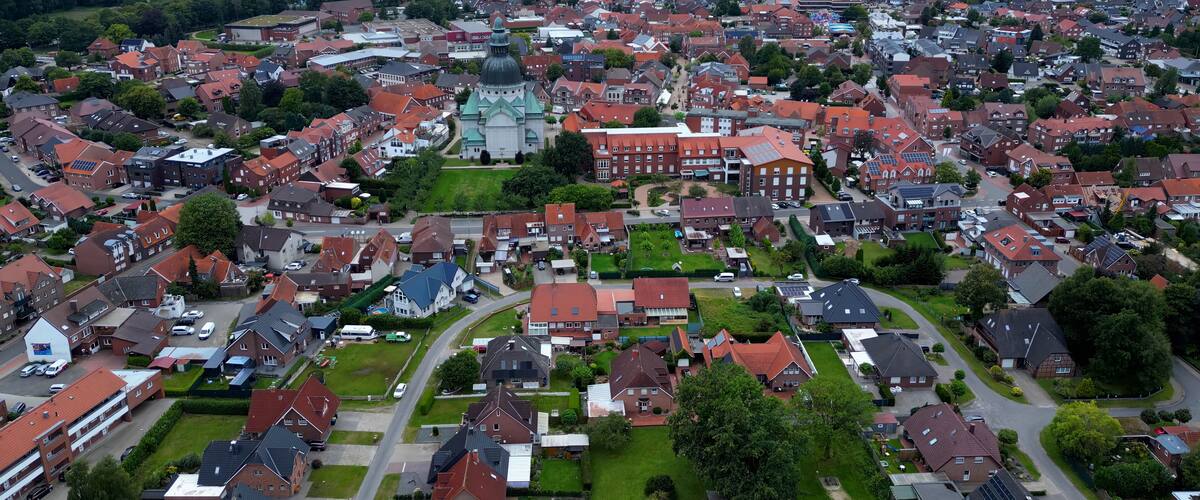 An aerial view of a densely populated residential area with red-roofed houses, a prominent church, and a large industrial building.