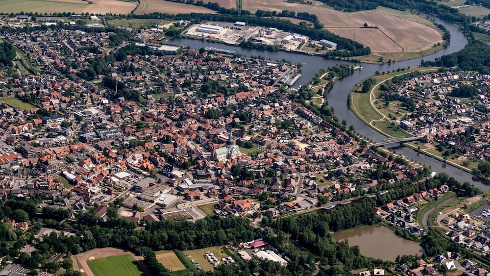 An aerial view of a town with a river, green fields, and a bridge.