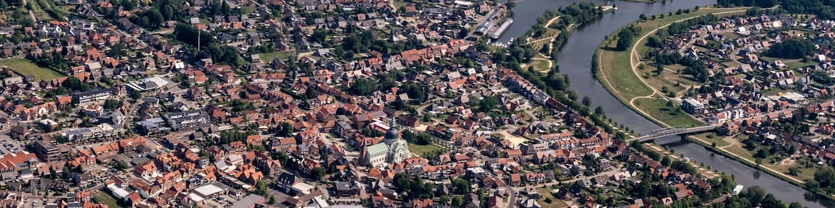 An aerial view of a town with a river, green fields, and a bridge.
