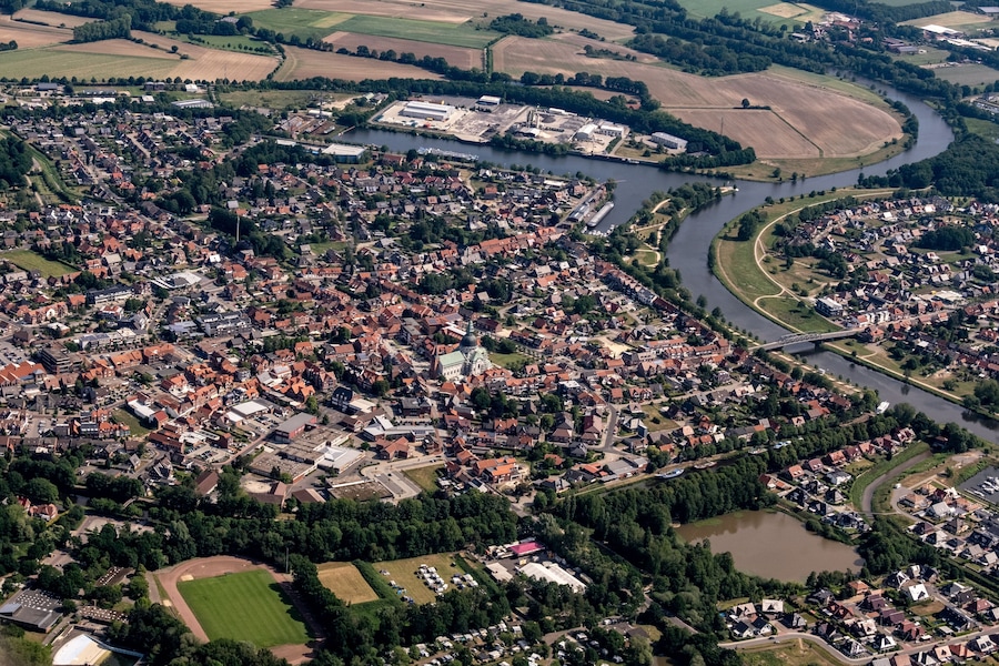 An aerial view of a town with a river, green fields, and a bridge.