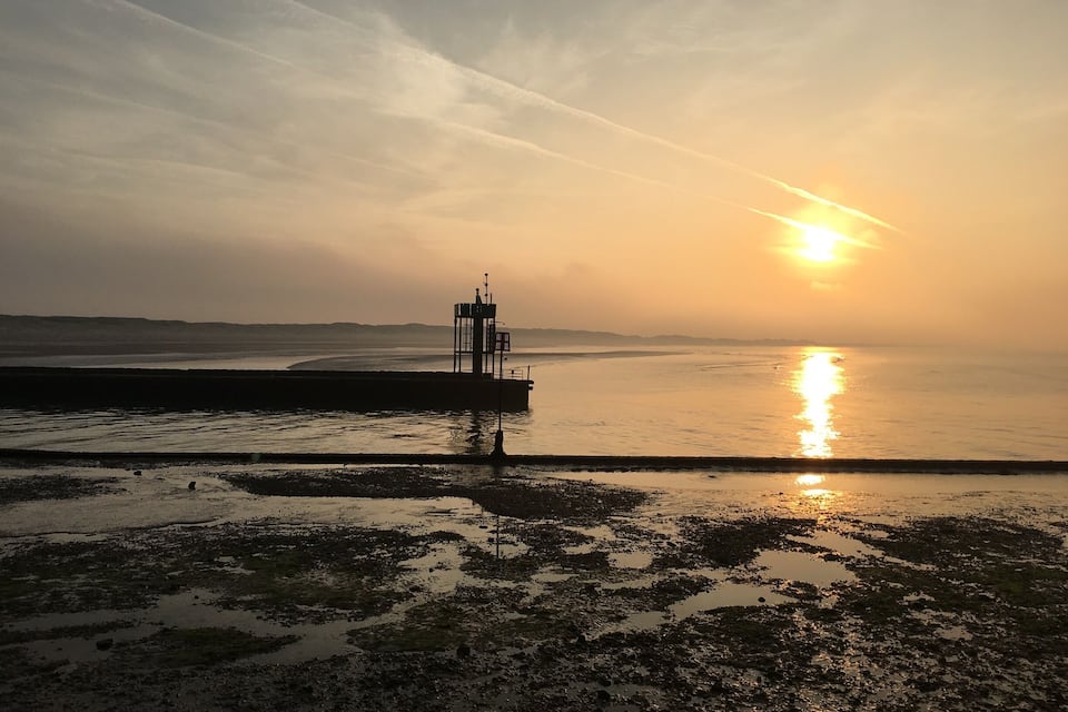 Un atardecer sobre un mar tranquilo con un faro a lo lejos.