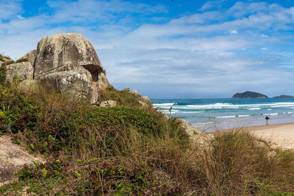 A beach with rocky outcrops, a sandy shore, and distant mountains under a partly cloudy sky.