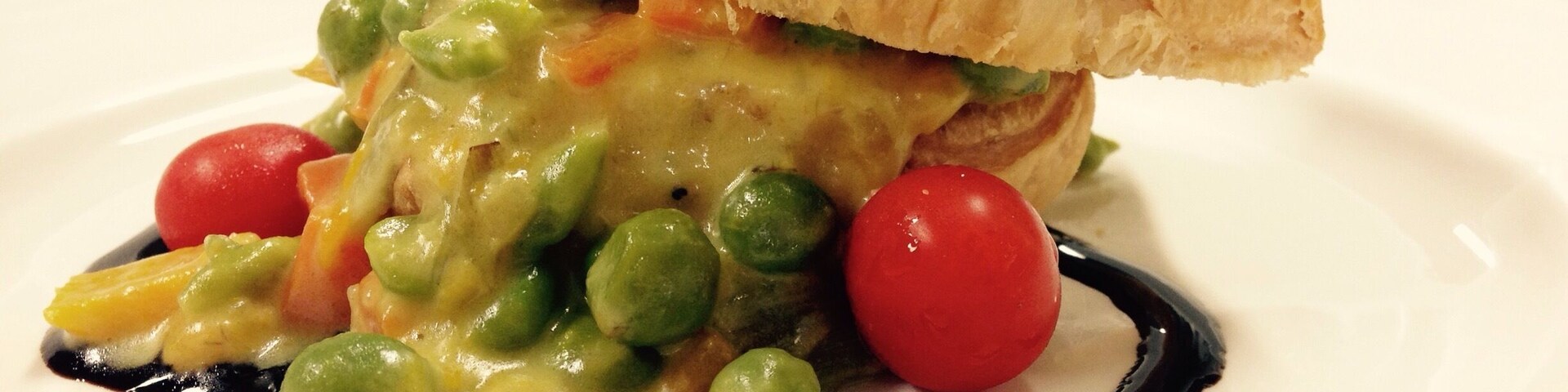 Un plato con un bollo de pastelería, guisantes, zanahorias y tomates cherry.