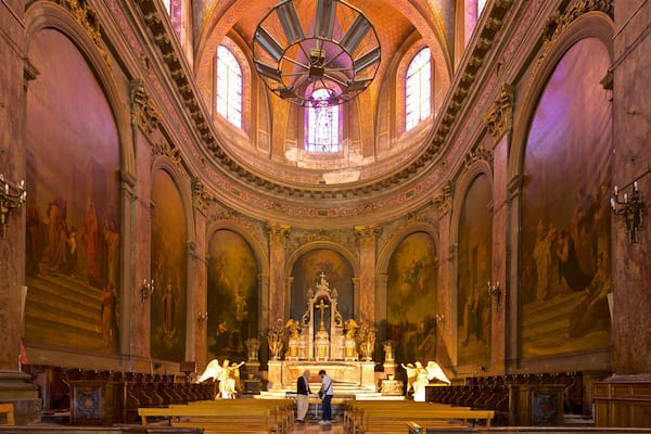 L’intérieur d’une église richement décorée, avec un autel central, des fenêtres en arc de cercle et des statues religieuses.