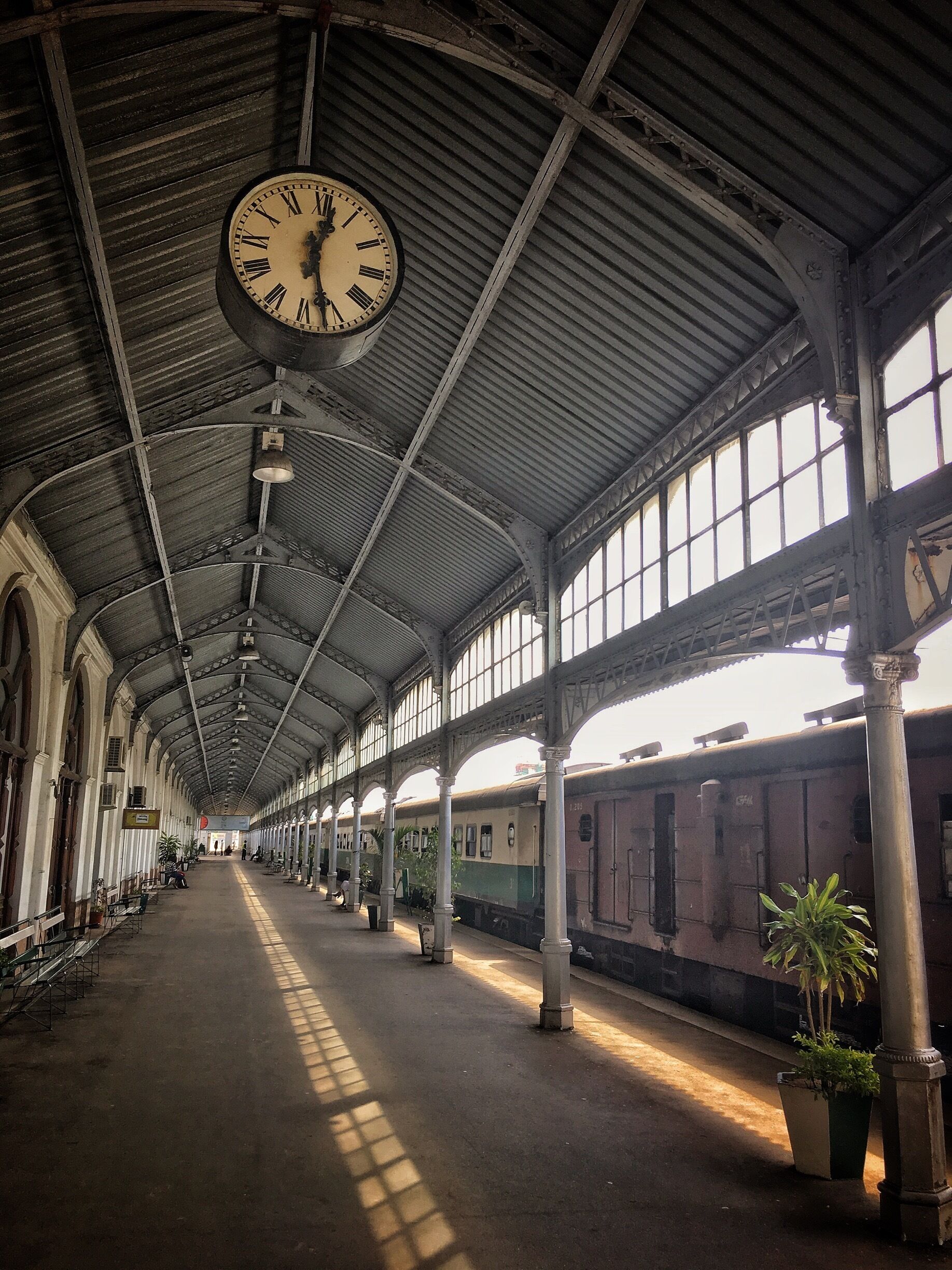 Uma estação de trem antiga com um relógio grande, tetos altos e luz do sol entrando pelas janelas.