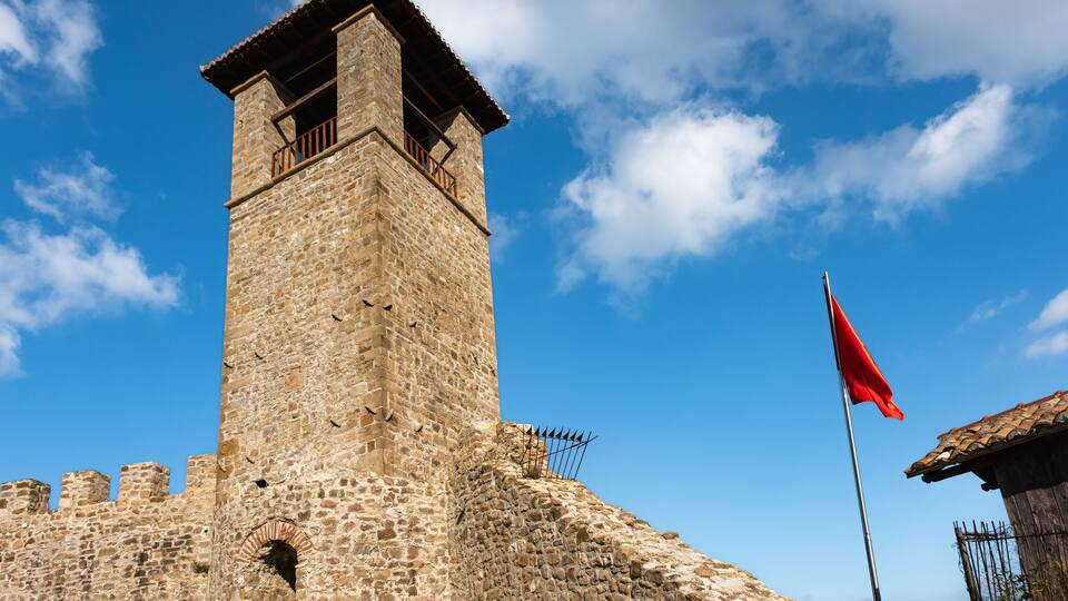 Clock Tower of Preze Castle, Tirana with albanian flag on blue sky background