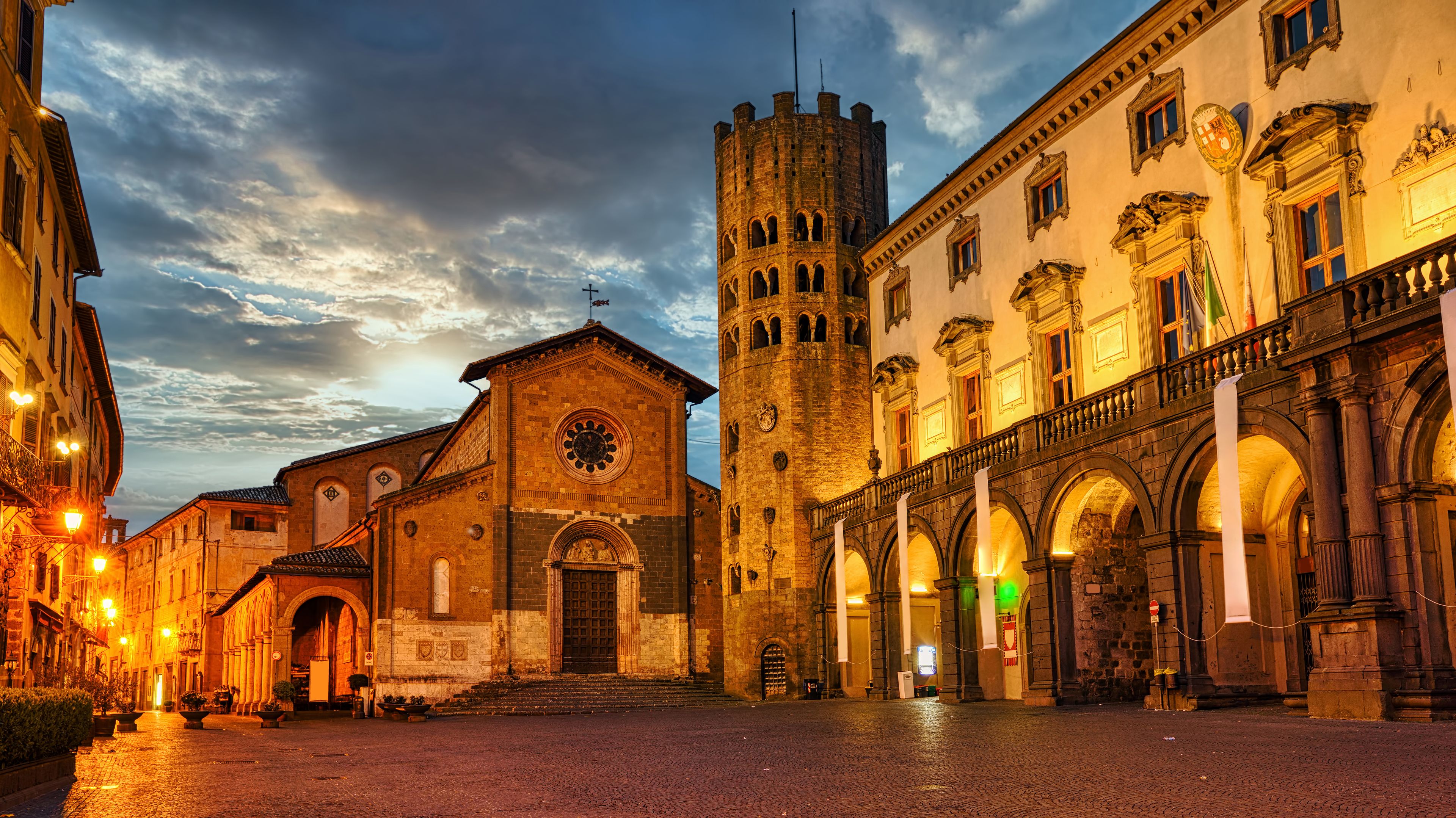 A historic square with a church, a castle, and ornate buildings under a twilight sky.