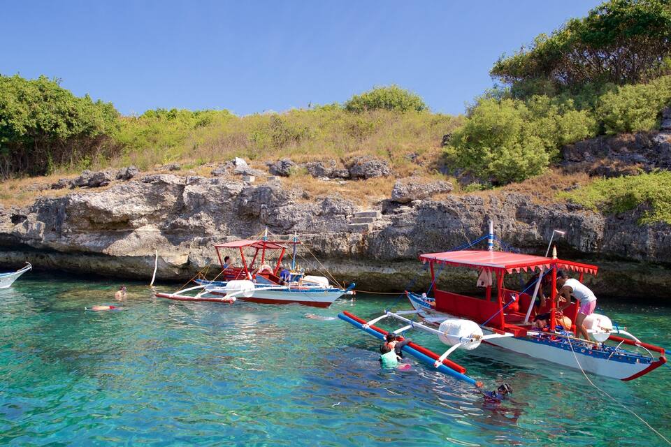 A clear blue sea with boats anchored near rocky cliffs.