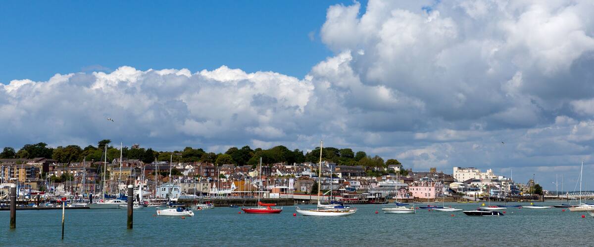 A harbor with numerous boats, a town in the background, and a partly cloudy sky.