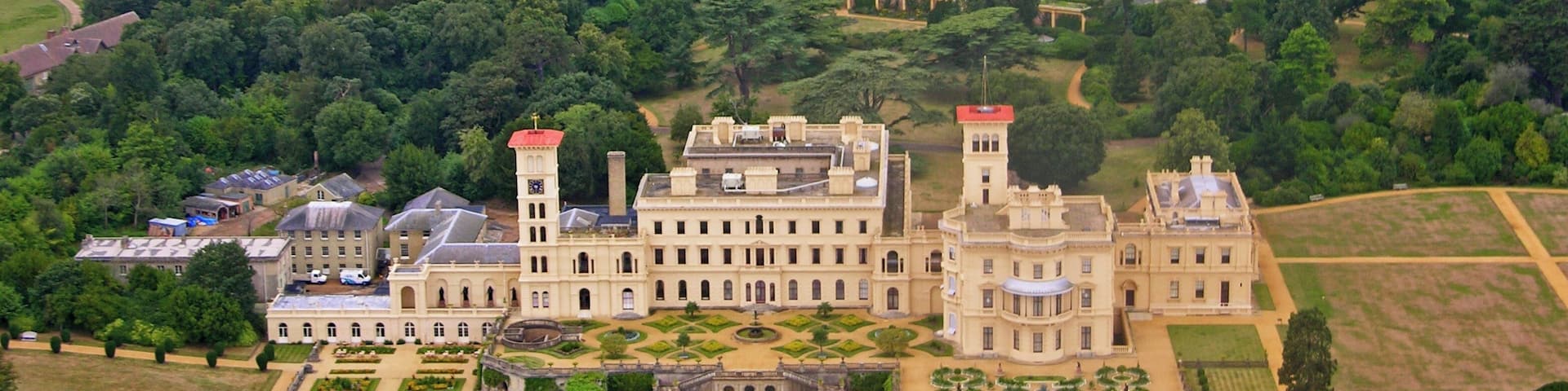 An aerial view of a large estate with a central building featuring two towers, surrounded by manicured gardens and fields.