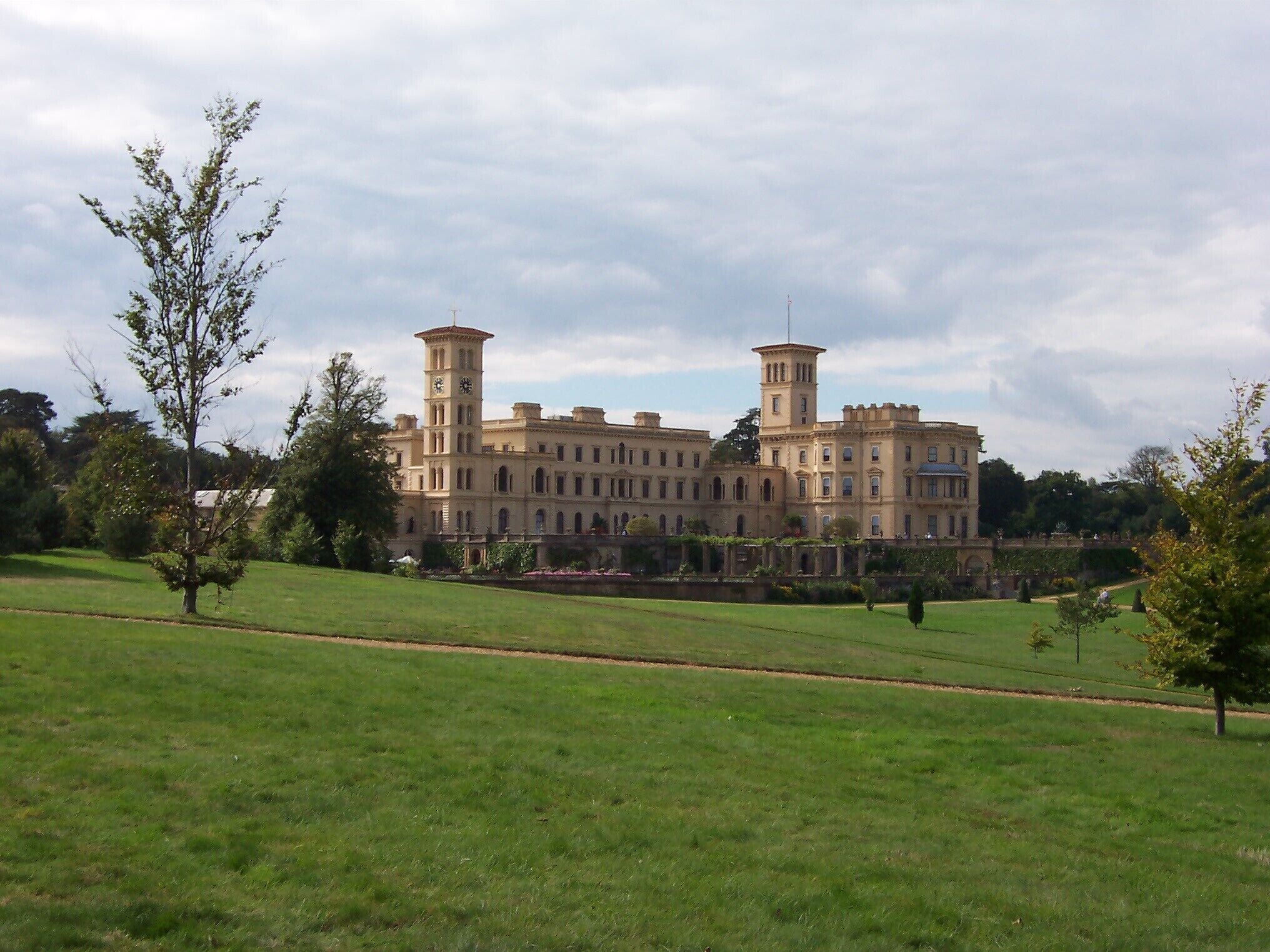 A large, historic building with two towers and a well-maintained lawn in the foreground.