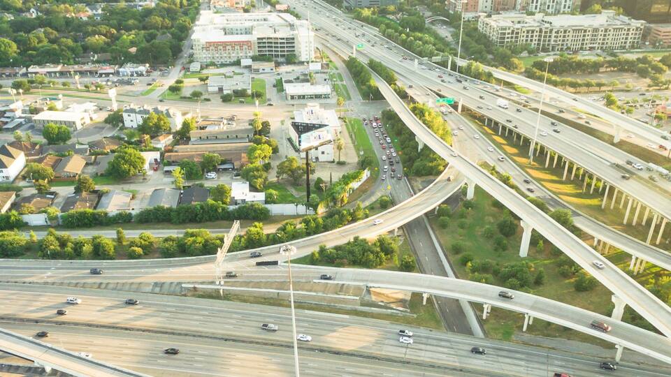 Ein komplexer Autobahnknotenpunkt mit mehreren Brücken und einem Wohngebiet mit Häusern und Grünflächen.