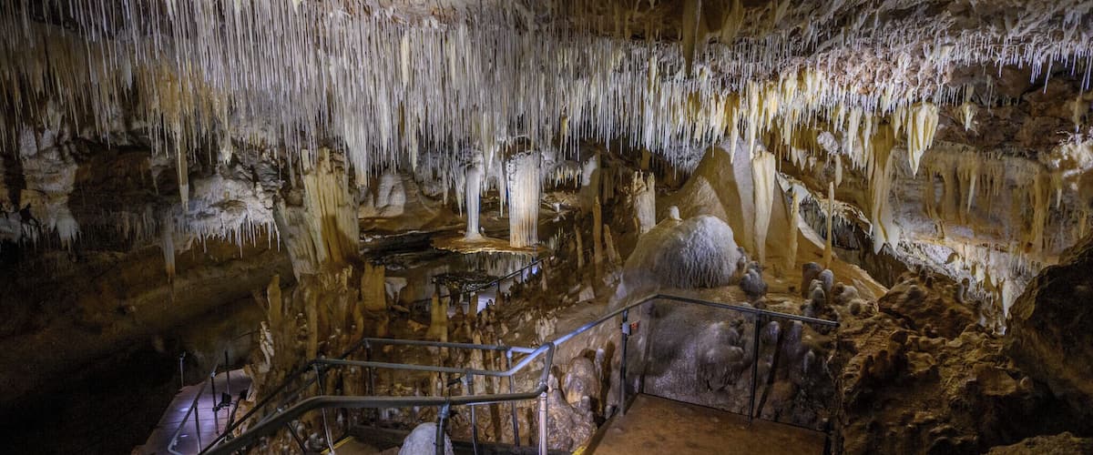 A cave with stalactites and stalagmites, metal railings, and a staircase.