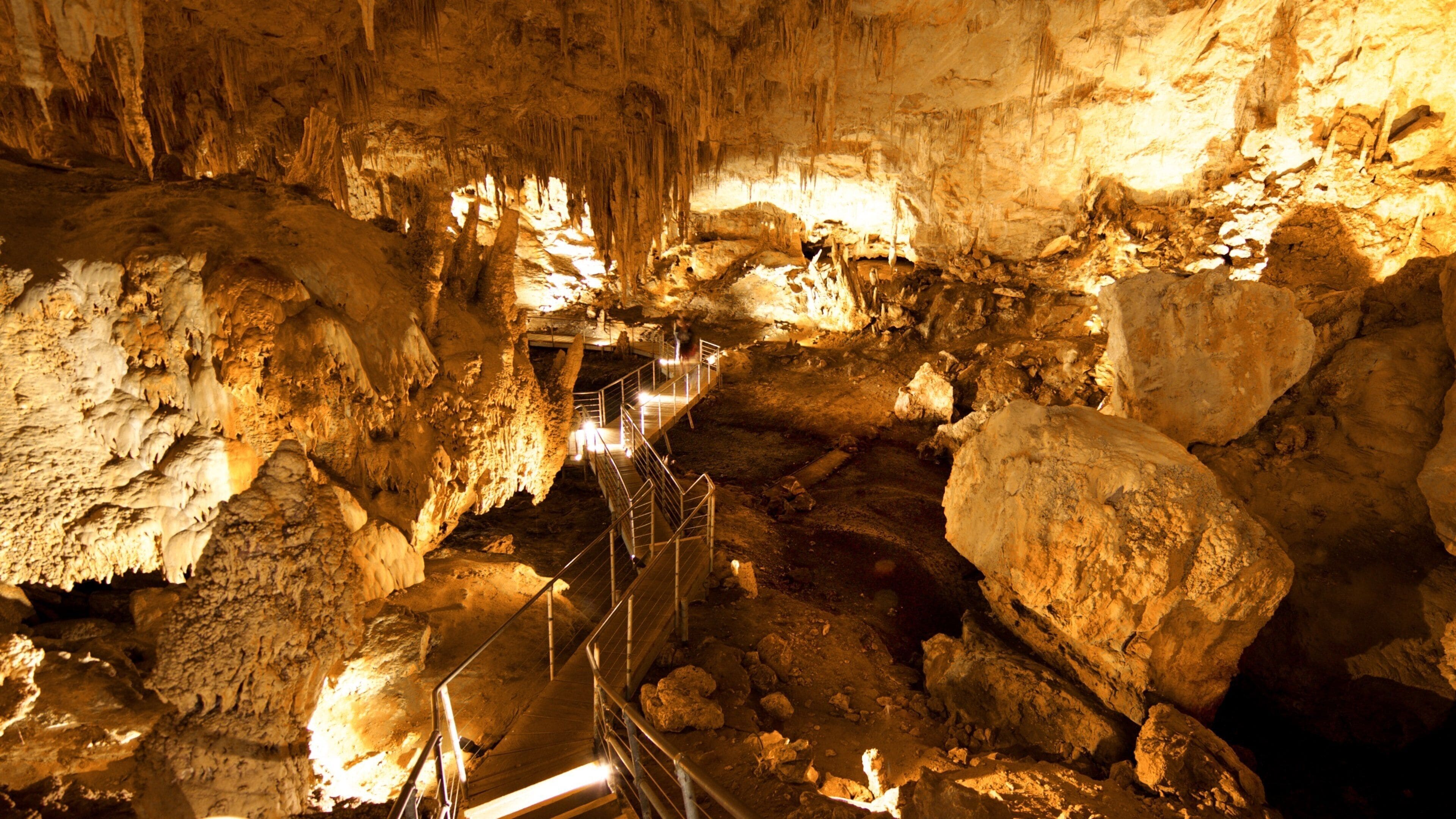 Una cueva con estalactitas y estalagmitas, un pasillo de metal y una gran formación rocosa.