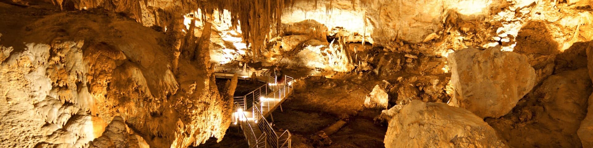 A cave with stalactites and stalagmites, a metal walkway, and a large rock formation.