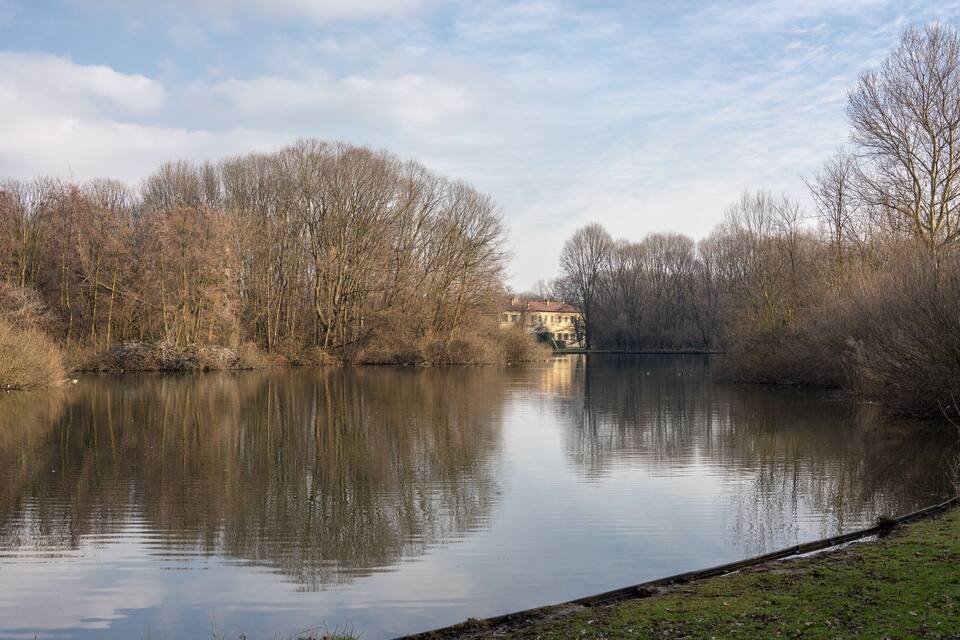 A calm river with a house on the opposite bank and leafless trees around.