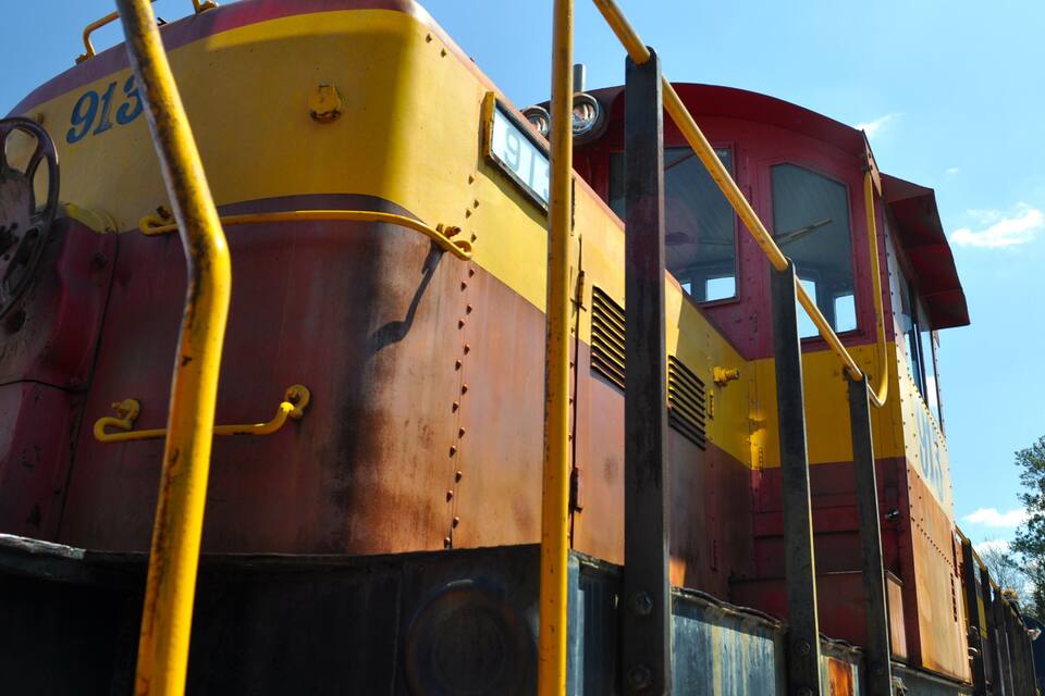 Une locomotive rouillée portant le numéro 915, aux couleurs jaune et rouge, et dotée d’une rambarde jaune.