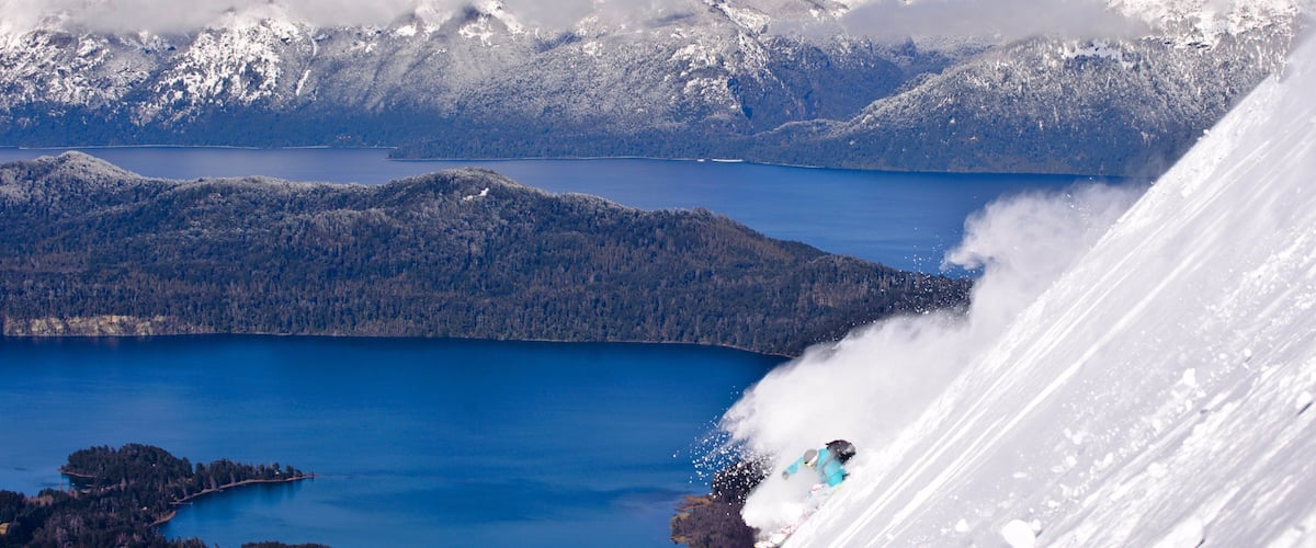A snowy mountain landscape with a lake and a skier in motion.