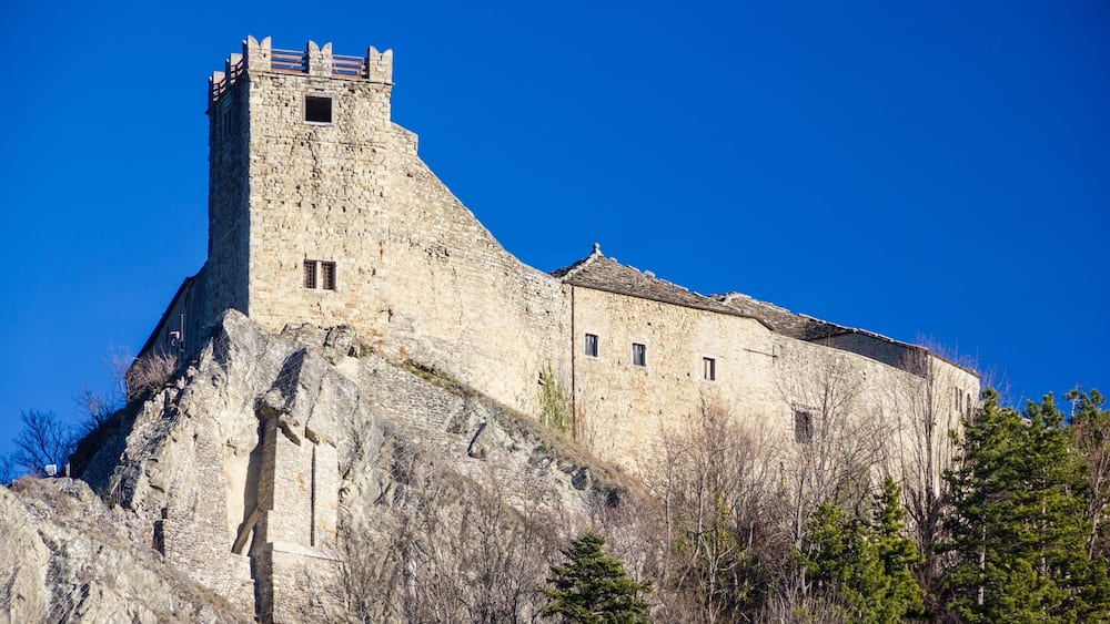 Un château de pierre historique, perché sur une colline, sous un ciel d’un bleu éclatant.