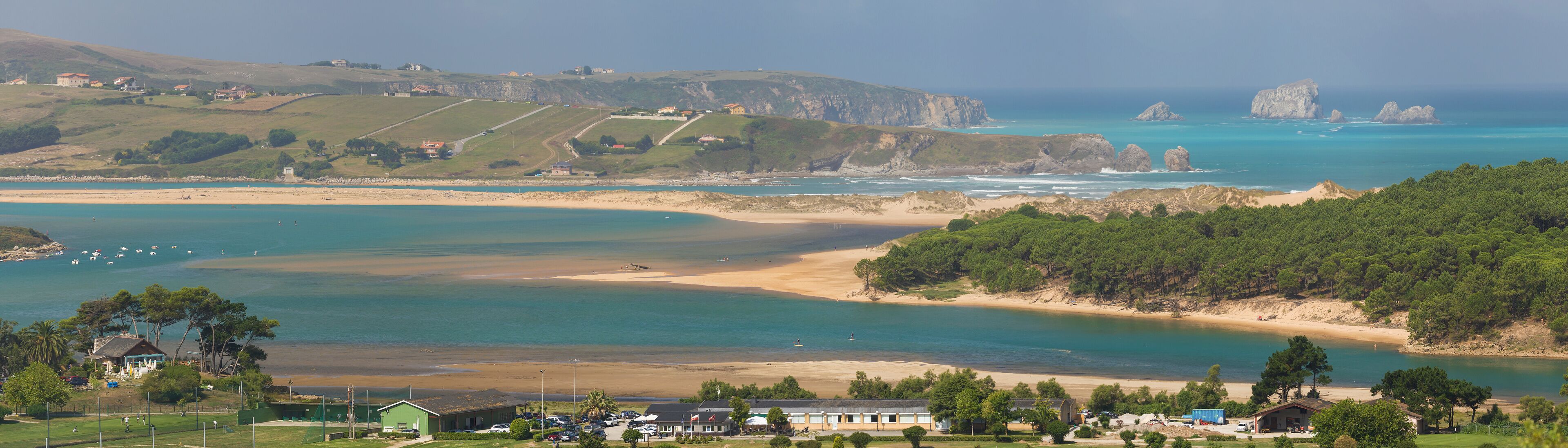 A coastal landscape with a sandy beach, clear turquoise waters, and rocky cliffs.
