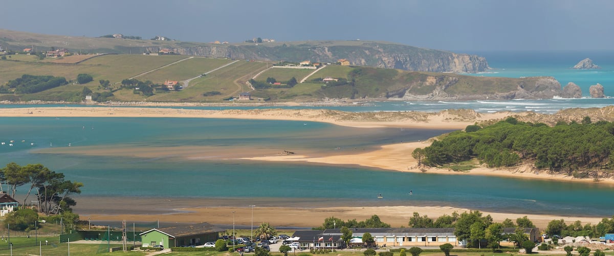 A coastal landscape with a sandy beach, clear turquoise waters, and rocky cliffs.